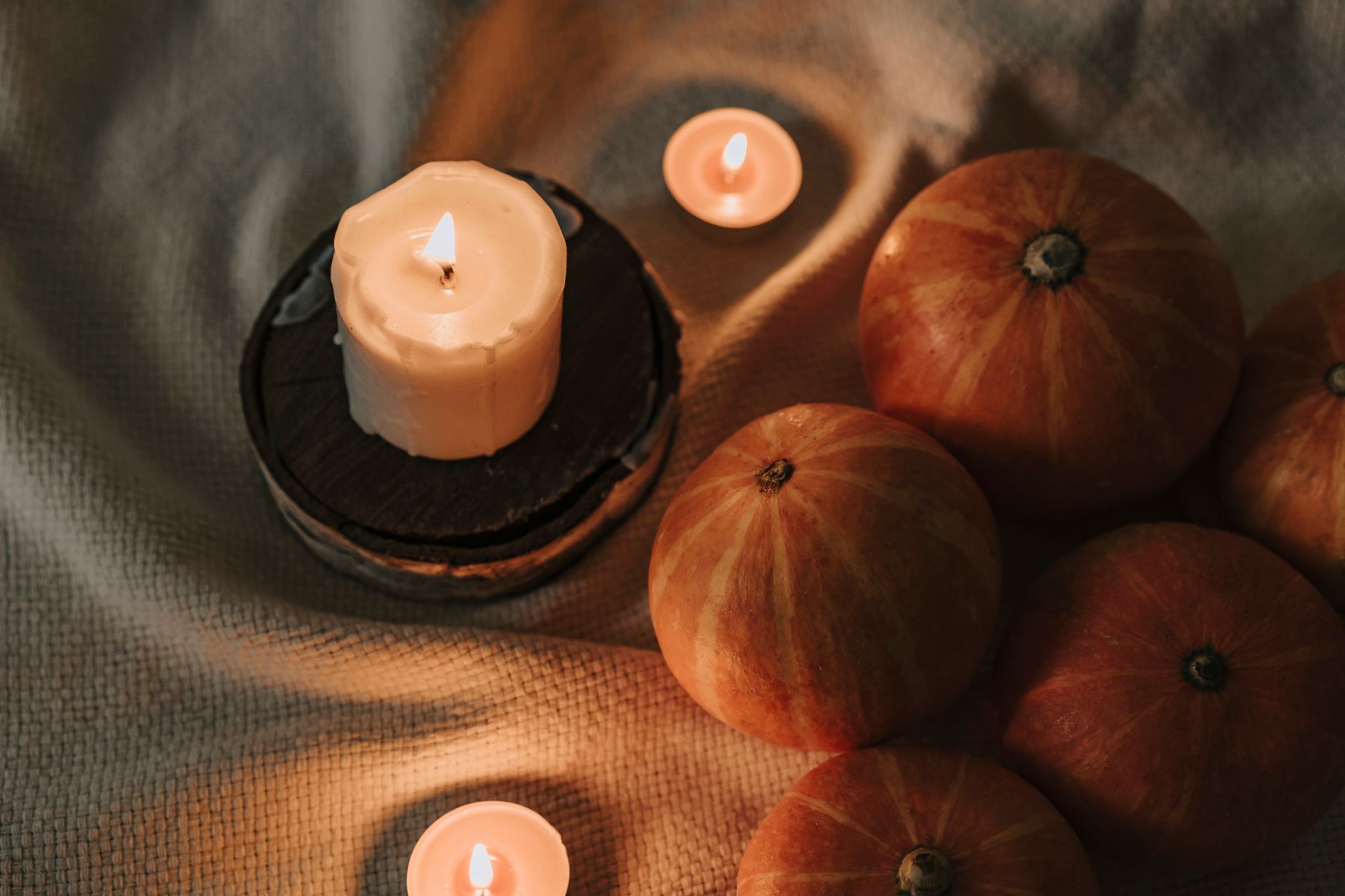 Lit candles and small pumpkins arranged on soft fabric in warm light
