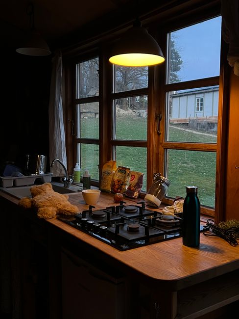 A warm kitchen at twilight, lamplight in the window